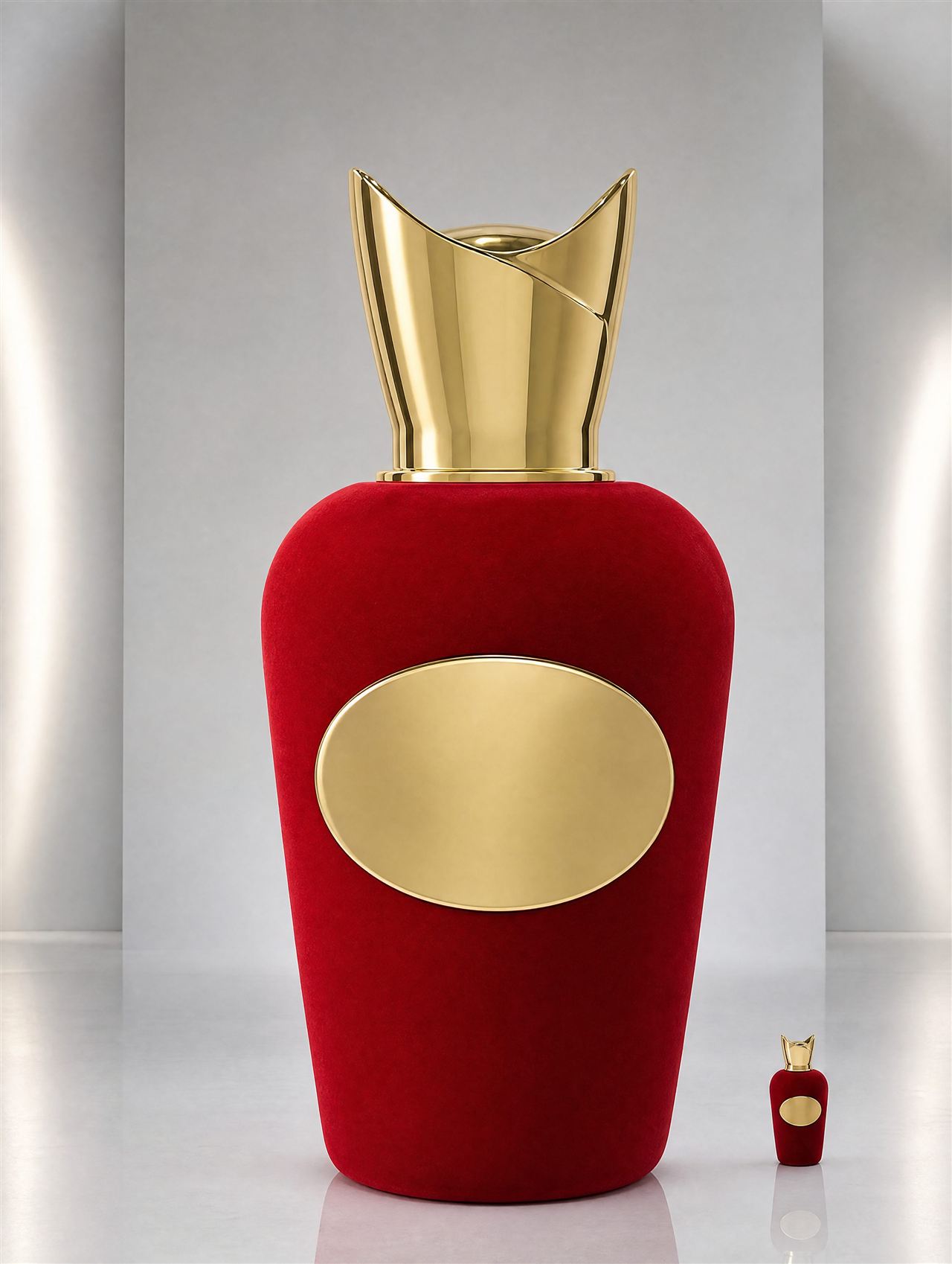 Oversized red velvet-flocked perfume bottle display model with a polished gold cap, standing beside an original-size bottle
